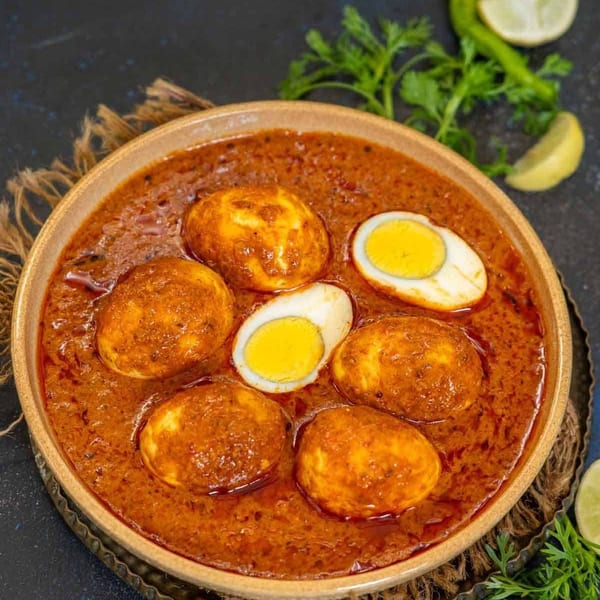 A bowl of Indian egg curry with whole and halved boiled eggs in a rich, reddish-brown gravy.