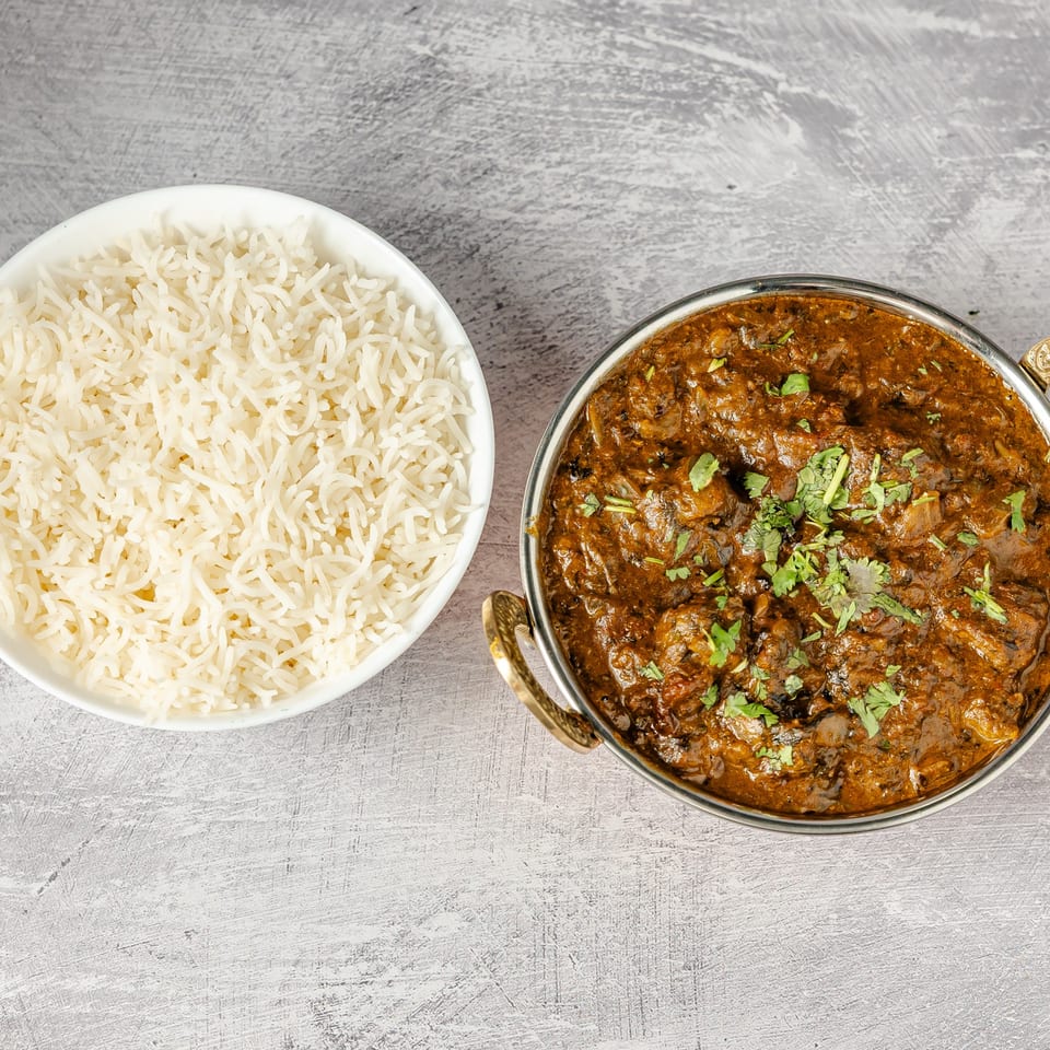 Bowl of basmati rice beside a richly spiced curry garnished with fresh cilantro on a gray tabletop.