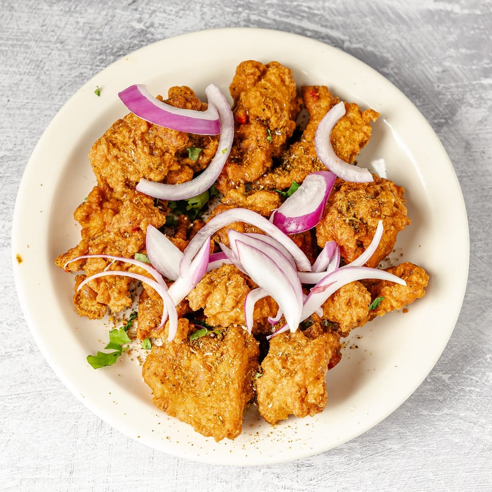 Crispy golden fried pieces garnished with sliced red onions, herbs, and spices on a white plate.