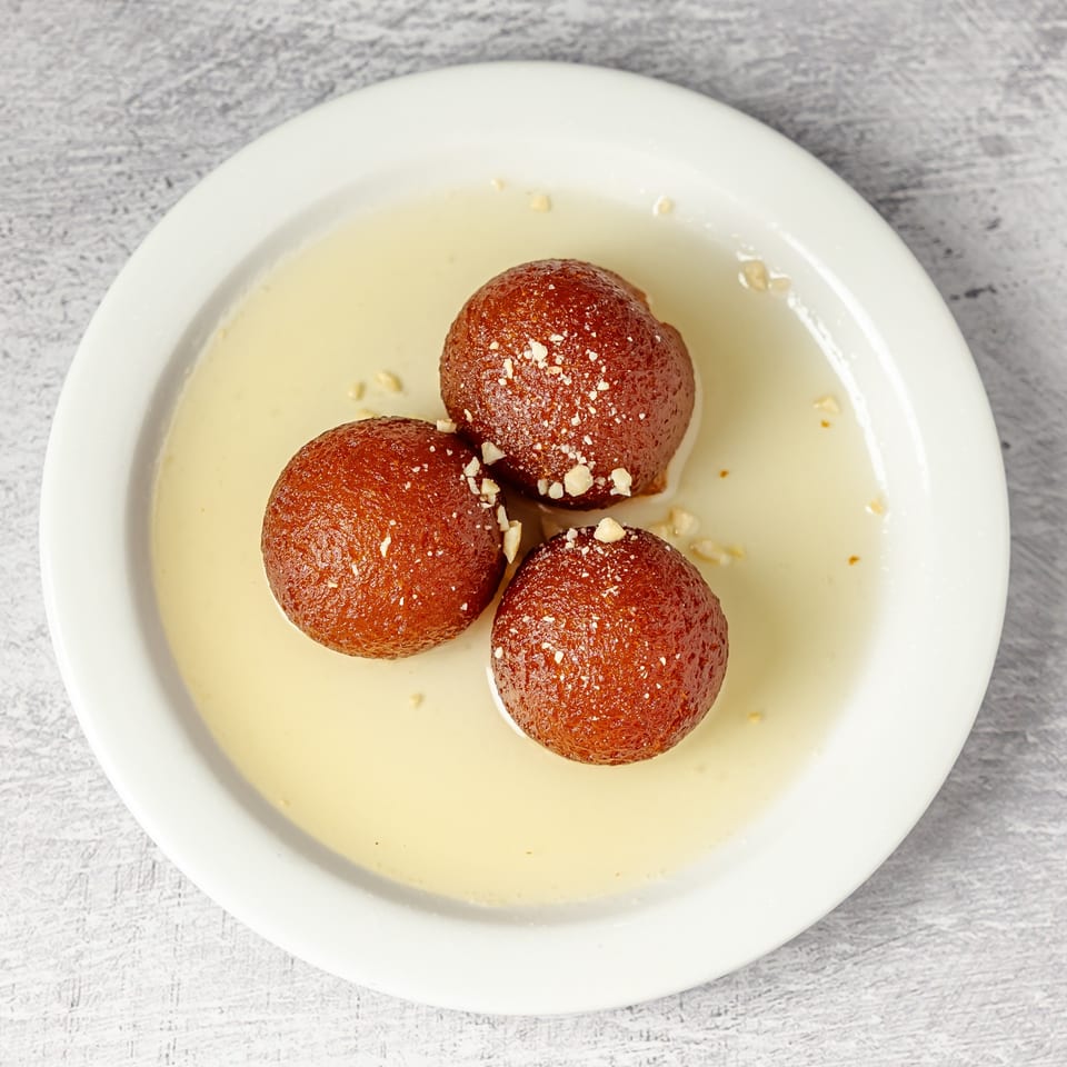 Three syrup-soaked brown dessert balls topped with chopped nuts on a white plate.