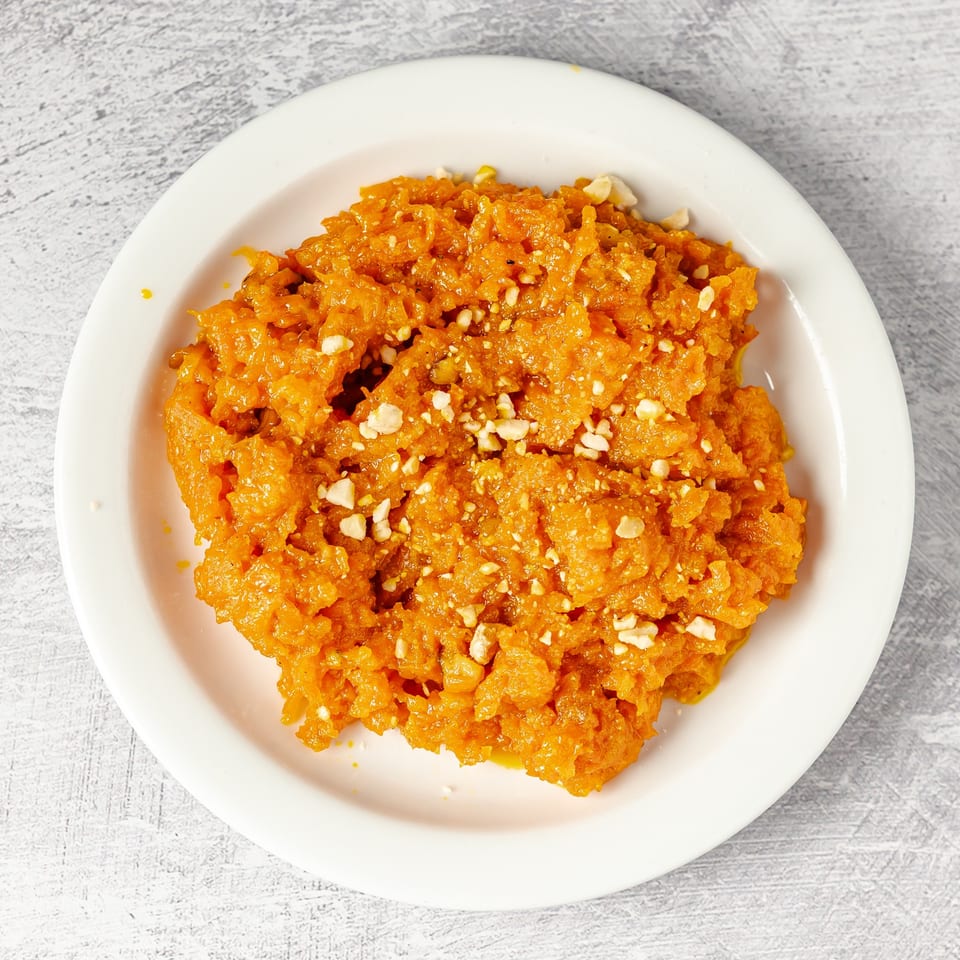 Golden-orange shredded dessert topped with crushed nuts, served on a white plate.