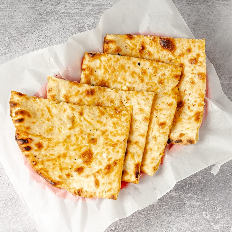 Golden-brown grilled flatbread pieces arranged on white parchment paper over a weathered gray tabletop.