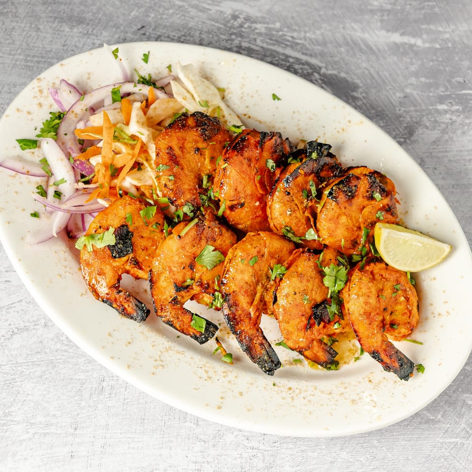 Grilled orange-marinated chicken pieces garnished with cilantro, served with sliced onions, shredded vegetables, flatbread, and lemon.