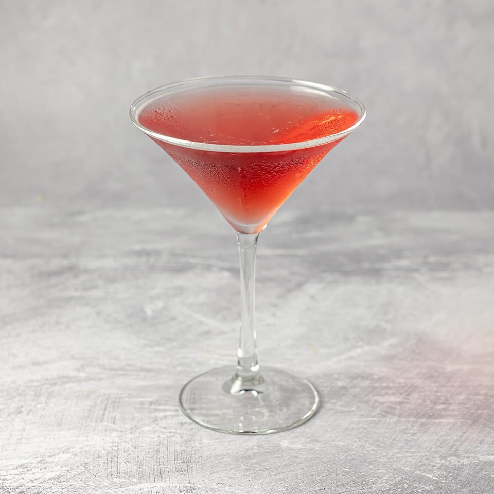 Red cocktail served in a chilled martini glass on a light gray tabletop.