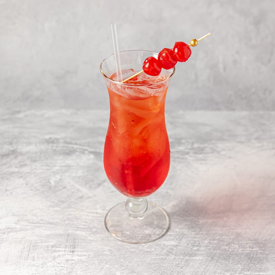 Red iced cocktail in a stemmed glass with a straw and cherry skewer garnish on a light tabletop.