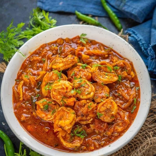 A white bowl filled with shrimp curry, garnished with fresh cilantro, on a dark surface.