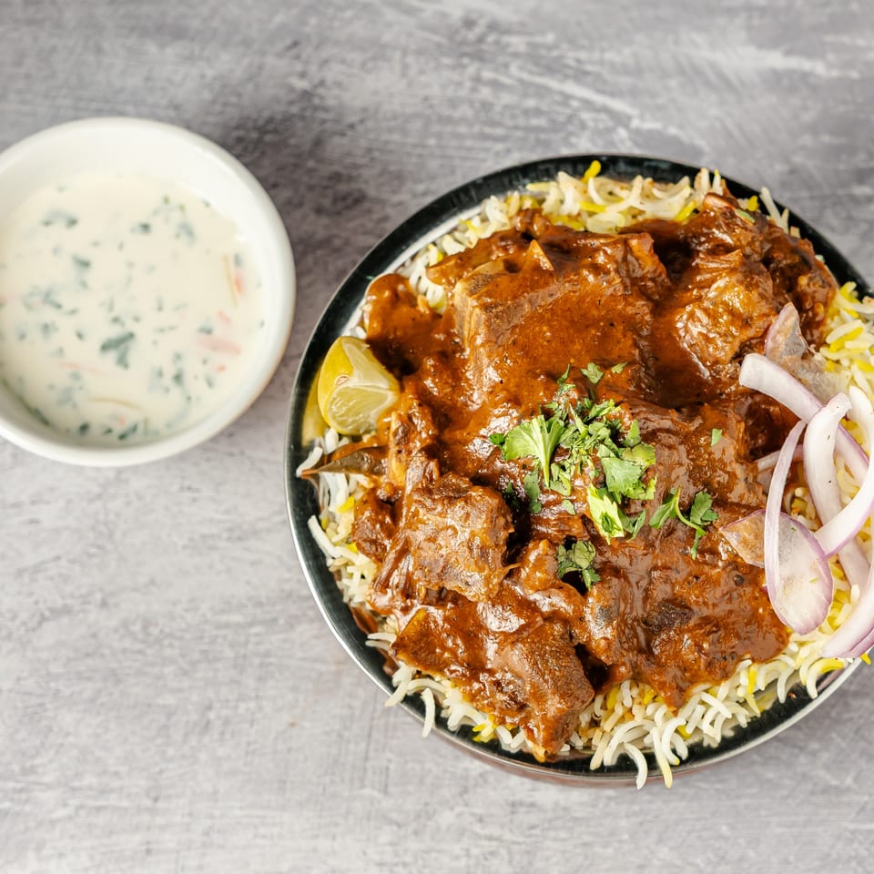 Spiced meat in rich curry sauce served over basmati rice, garnished with cilantro, onions, lime, and creamy herb sauce.