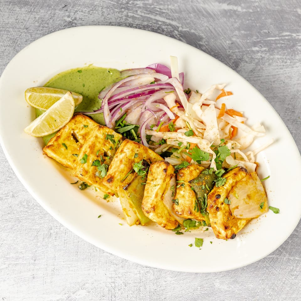 Grilled spiced paneer and vegetables garnished with cilantro, served with lime wedges, creamy green sauce, and cabbage slaw.